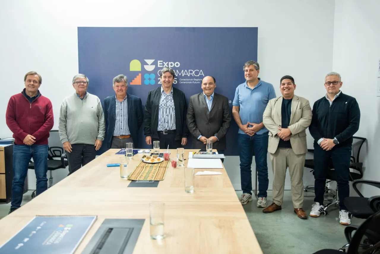 Ocho hombres posan parados detrás de una mesa de reuniones frente a un cartel de la Expo Catamarca.