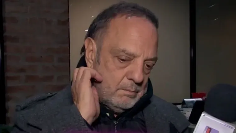Baby Etchecopar mirando hacia abajo y tocándose la oreja frente a un micrófono de prensa.