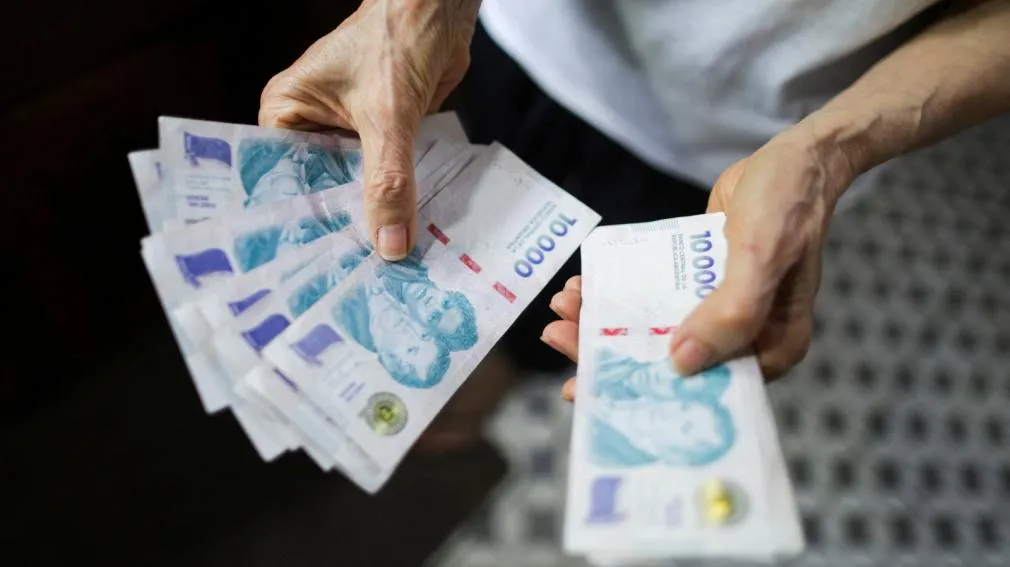 Una persona sostiene varios billetes argentinos de diez mil pesos entre sus manos.