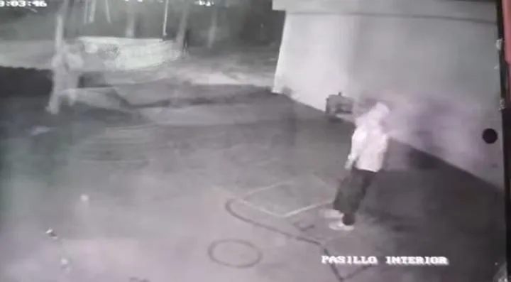 Captura de cámara de seguridad nocturna que muestra a una persona encapuchada en un patio o pasillo interior.