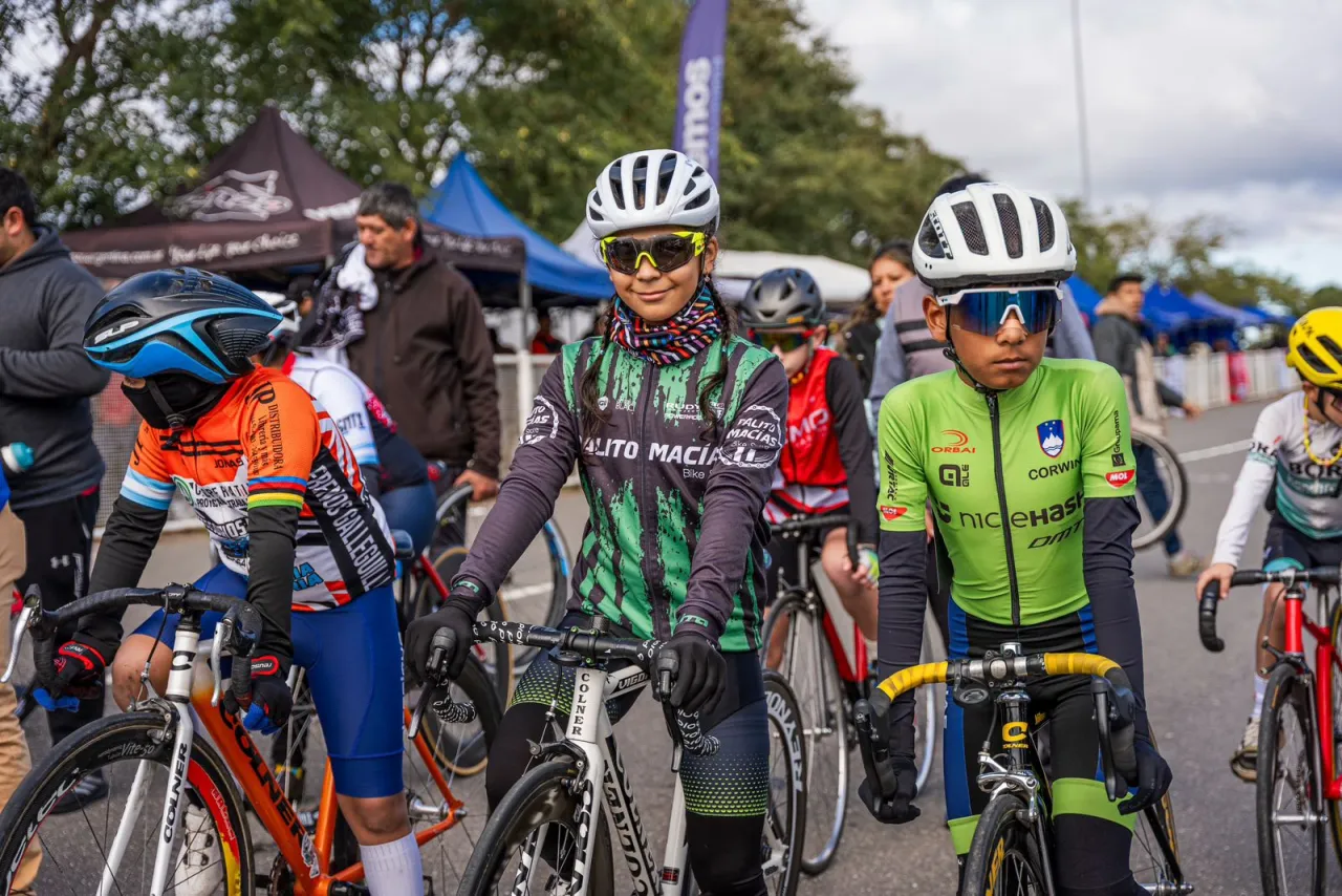 Varios chicos con cascos, anteojos y ropa deportiva están listos sobre sus bicicletas de carrera.