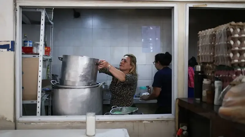 Dos mujeres cocinan con ollas de gran tamano en una cocina.
