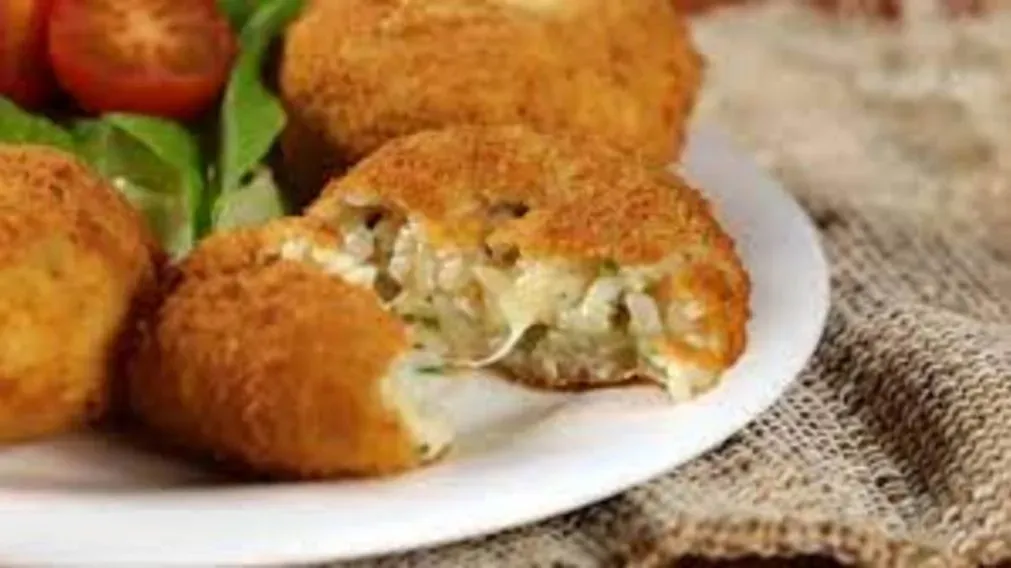 Croquetas de arroz fritas servidas en un plato blanco junto a lechuga y tomates cherry.