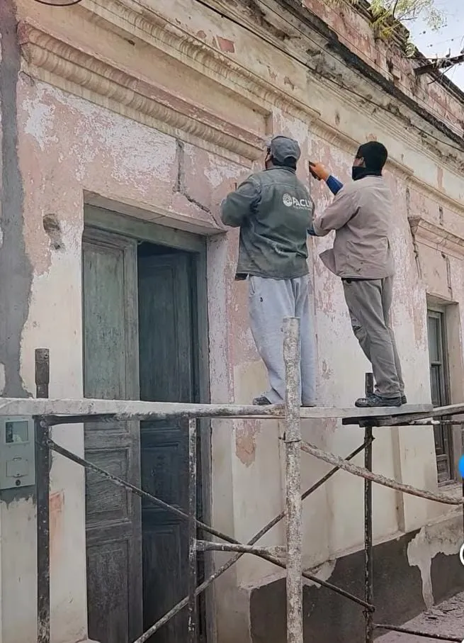 Dos obreros trabajan subidos a un andamio en la fachada deteriorada de un edificio antiguo.