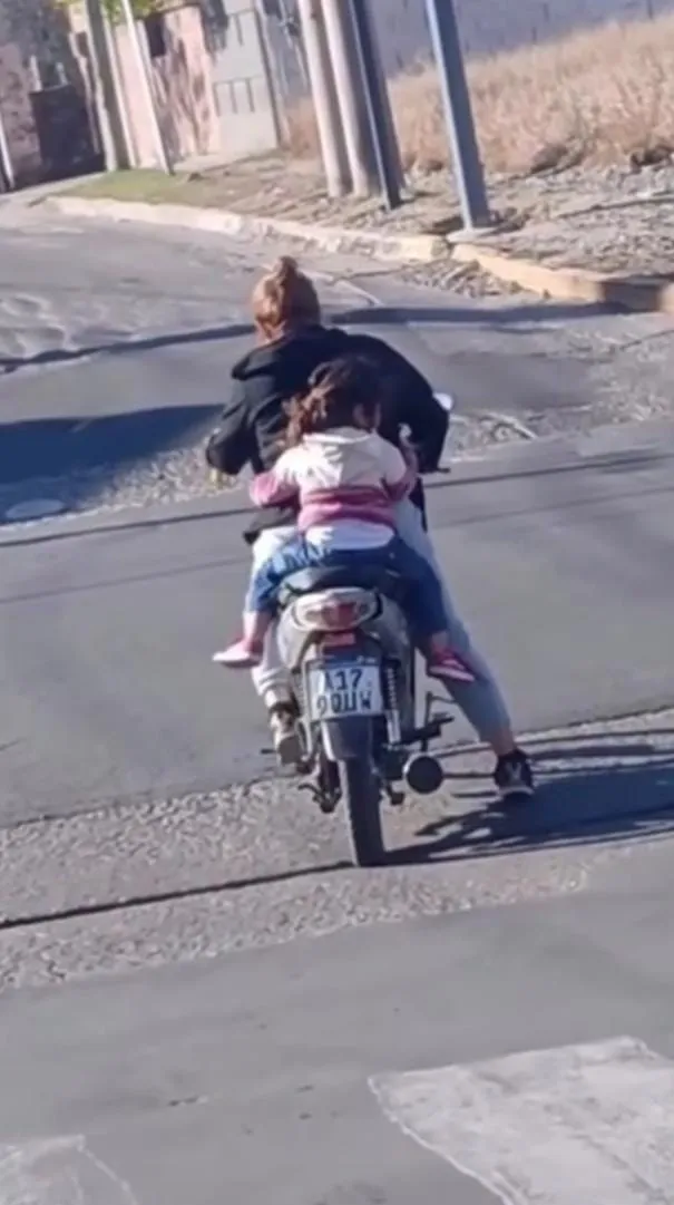 Dos personas van de espaldas en una moto por una calle asfaltada.