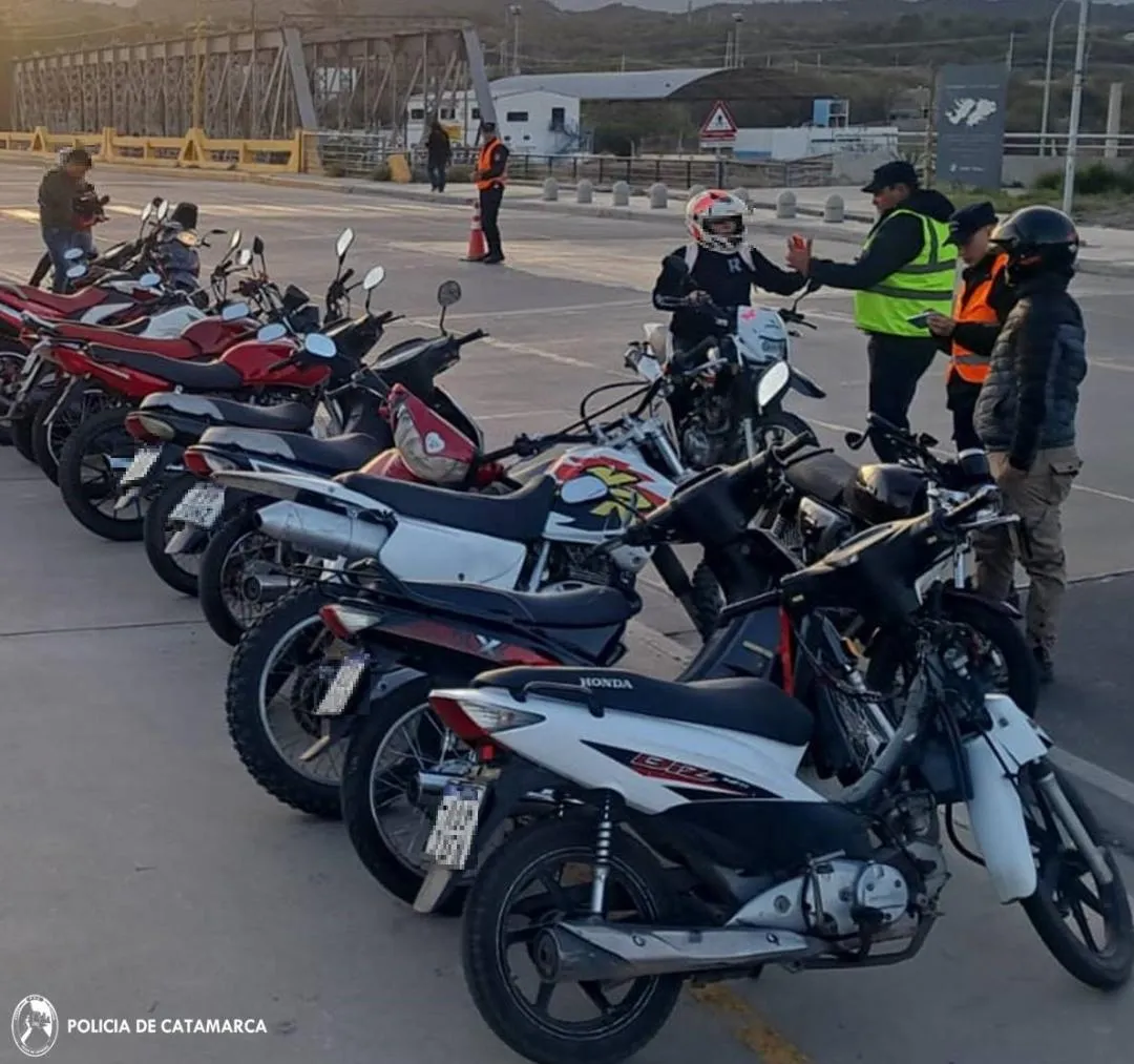 Efectivos policiales controlan a motociclistas junto a una fila de motos estacionadas sobre el pavimento.