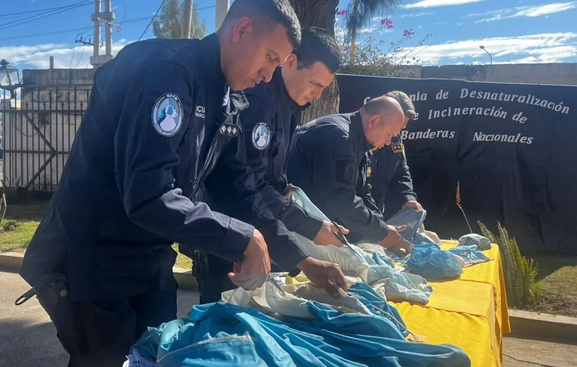Efectivos policiales cortan banderas celestes y blancas con tijeras sobre una mesa con mantel amarillo.
