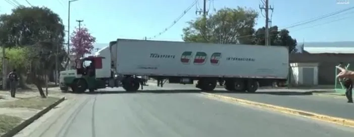 Un camión con semirremolque blanco cruzado de lado a lado sobre una calle de asfalto.
