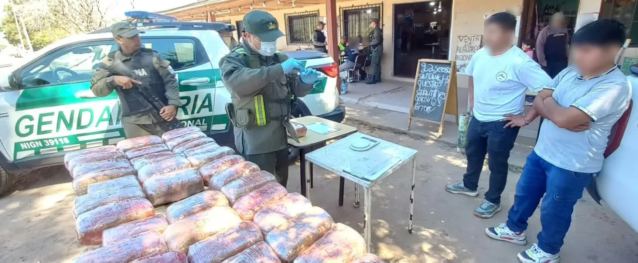 Gendarmes junto a un patrullero y una mesa llena de paquetes frente a dos personas de pie.
