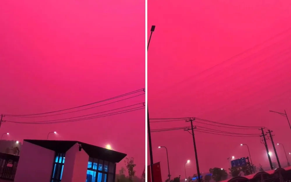 Un cielo completamente teñido de color magenta sobre un tendido eléctrico y edificaciones urbanas de noche.