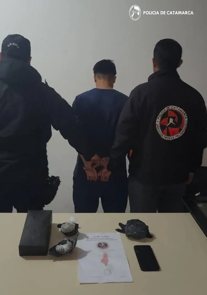 Dos efectivos policiales escoltan a un hombre esposado de espaldas frente a una mesa con elementos secuestrados.
