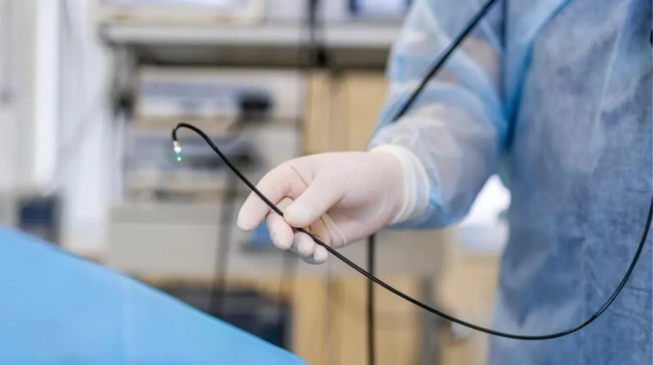 Una persona con guantes y camisolín médico sostiene el cable y la punta iluminada de un endoscopio.