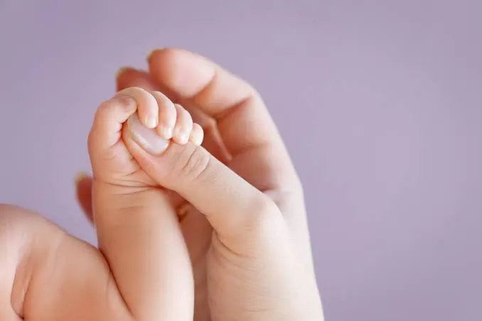 La mano de un bebé sostiene con fuerza el dedo pulgar de la mano de un adulto.