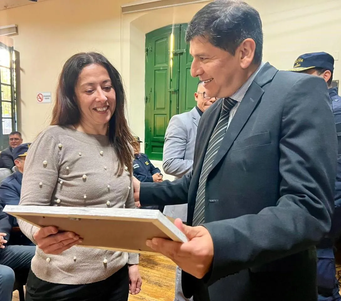 Un hombre de traje le entrega un cuadro a una mujer sonriente en una sala con público.