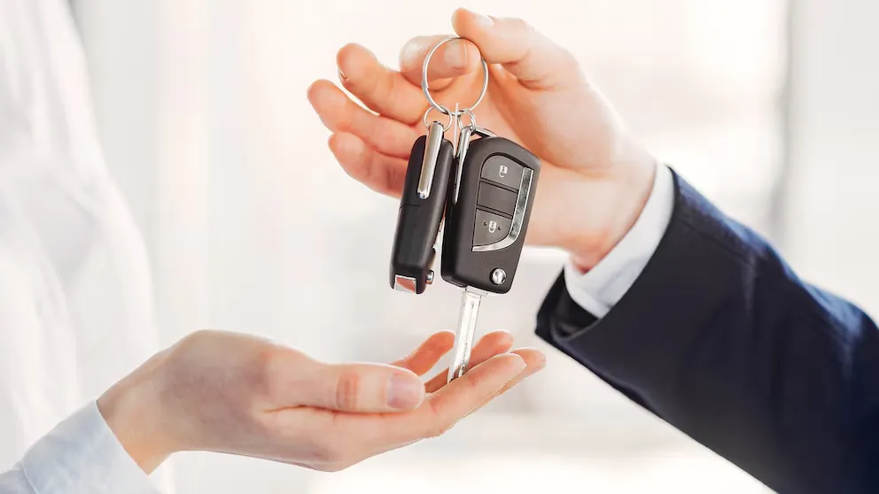 Una persona le entrega las llaves de un auto en la mano a otra.