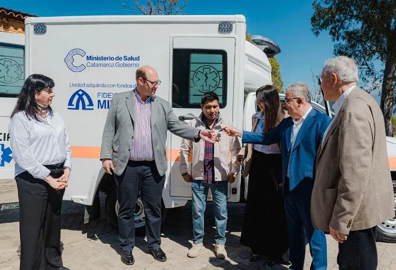 Un grupo de personas realiza la entrega de una llave frente a una ambulancia blanca.