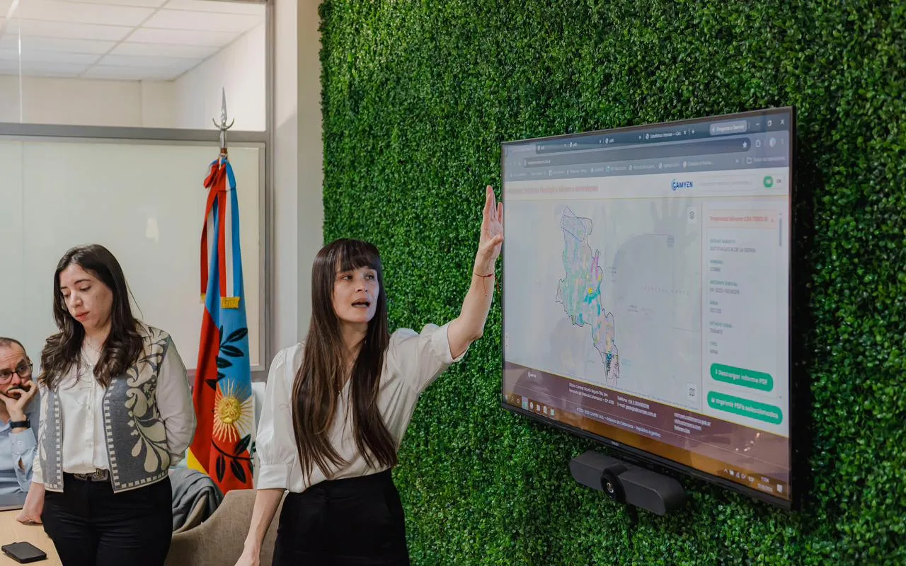 Una mujer señala un mapa en una pantalla de televisión junto a la bandera de Catamarca.