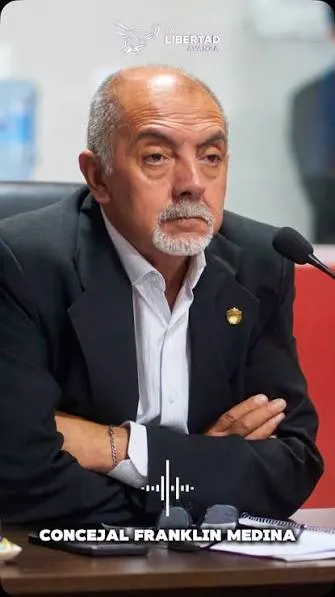 El concejal Franklin Medina está sentado con los brazos cruzados frente a un micrófono en una mesa de sesiones.