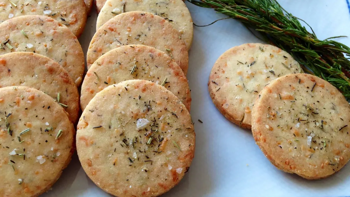 Galletitas saladas redondas con hierbas y granos de sal gruesa dispuestas sobre una fuente junto a ramitas de romero.