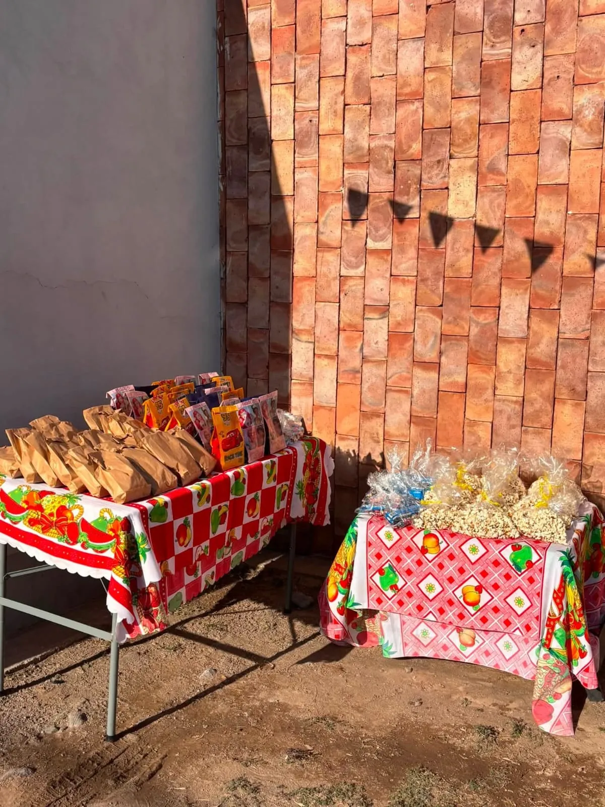 Dos mesas con manteles estampados exhiben bolsas de papel y paquetes con pochoclo frente a una pared de ladrillos.