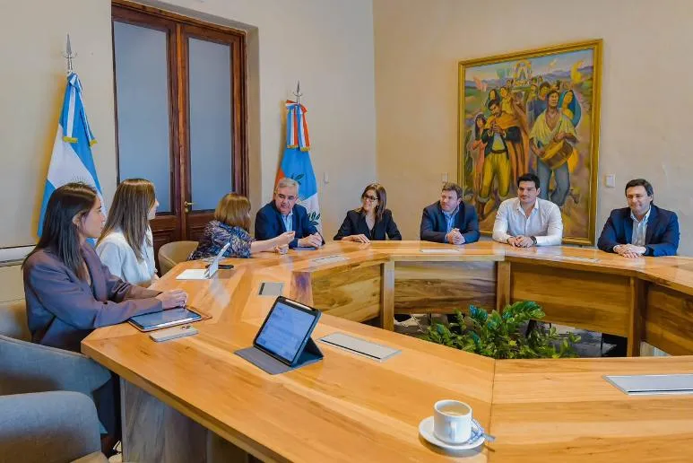 Raúl Jalil encabeza una reunión de trabajo junto a funcionarios alrededor de una gran mesa de madera.
