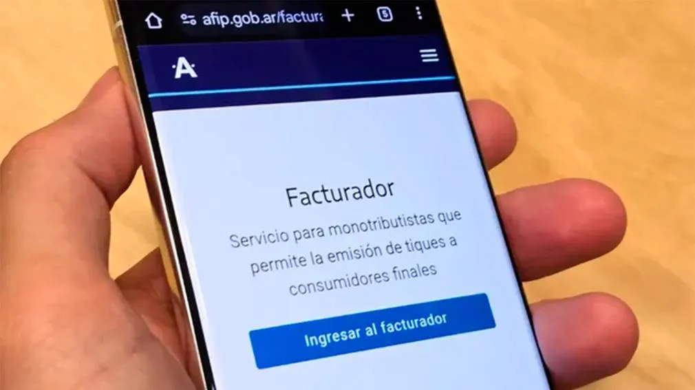 Una persona sostiene un teléfono celular que muestra en pantalla la aplicación del Facturador de AFIP.