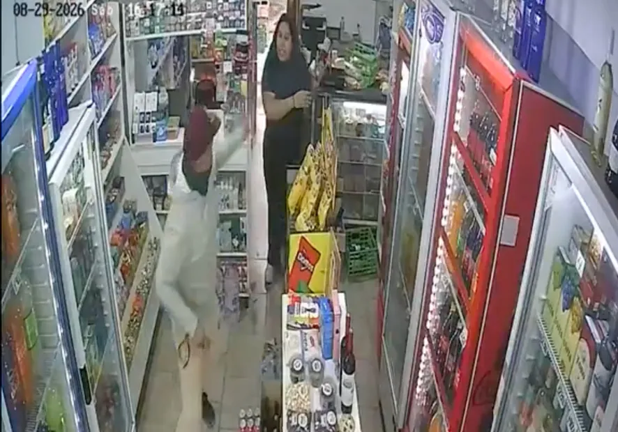 Una cámara de seguridad registra a una empleada y a un cliente en el pasillo de un almacén o kiosco.