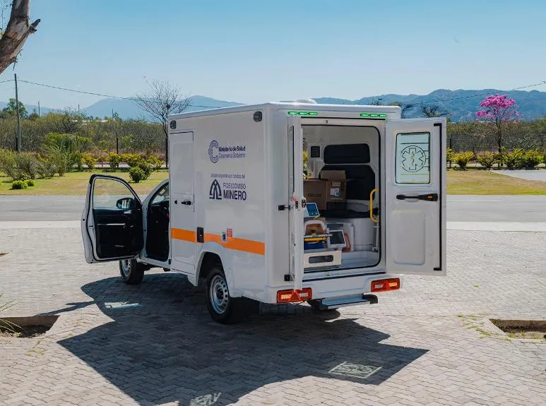 Una ambulancia blanca con las puertas abiertas estacionada en una calle de adoquines.