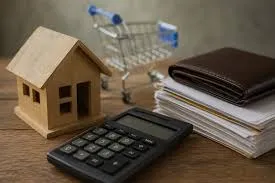Una calculadora, una casa en miniatura, un changuito de compras y papeles con una billetera sobre una mesa.