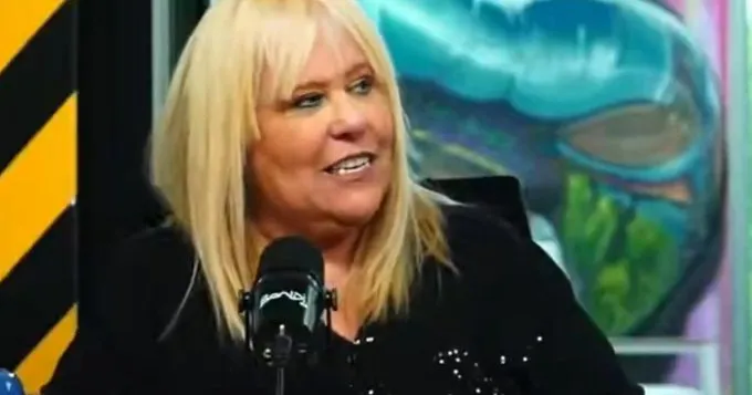 Una mujer rubia sonrie frente a un microfono en un estudio de grabacion o transmision.