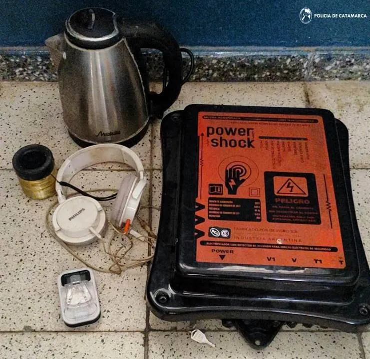 Una pava electrica, auriculares, un cargador universal y un electrificador de alambrados Power Shock sobre el piso.