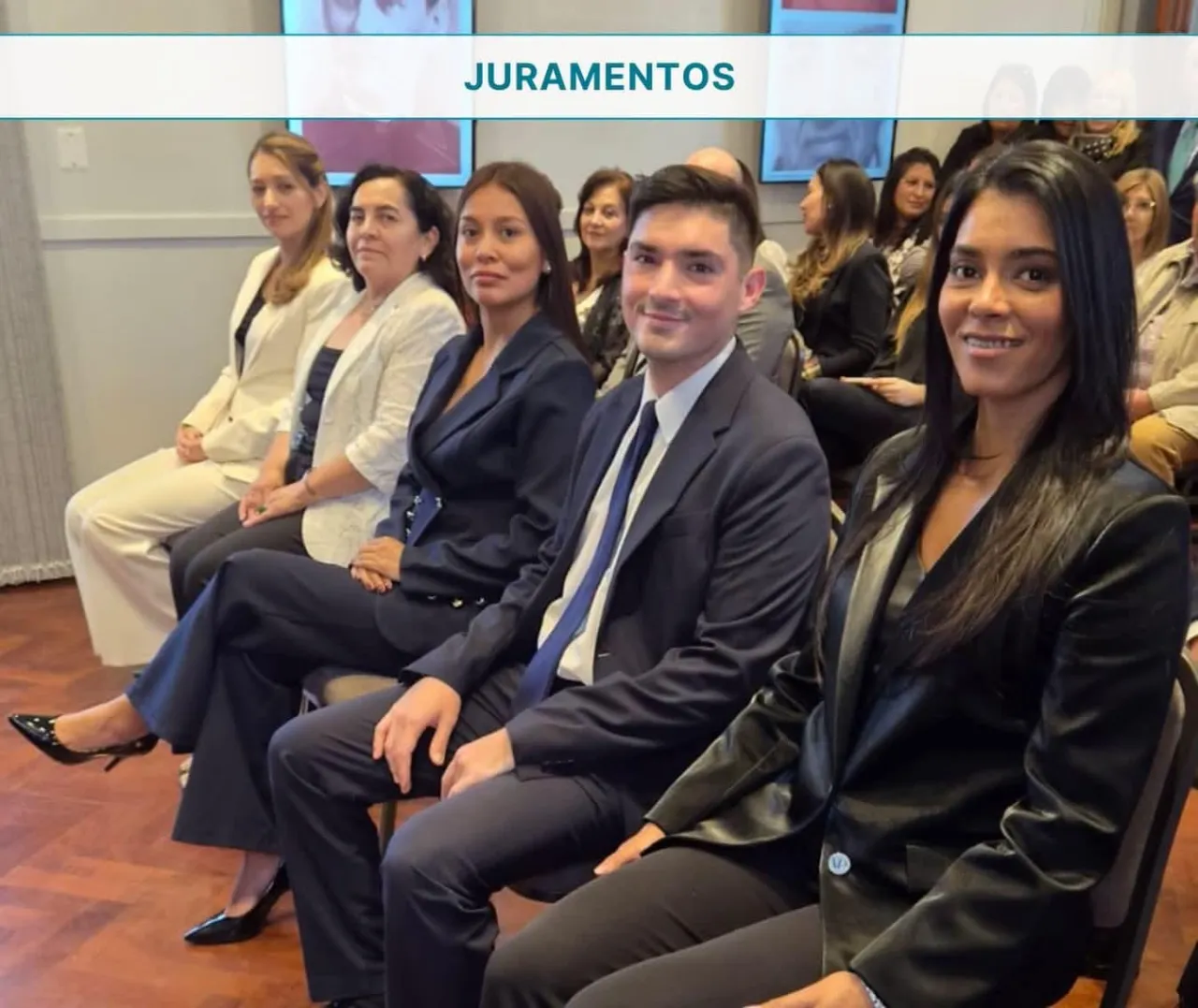 Un grupo de hombres y mujeres vestidos formalmente posan sentados en una sala bajo un cartel que dice juramentos.