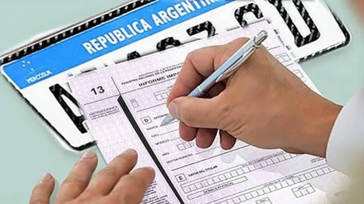 Una mano sostiene una lapicera sobre un formulario impreso, junto a una chapa patente de Argentina.