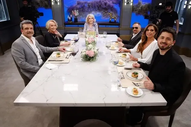 Mirtha Legrand preside una mesa larga rodeada por sus comensales en un estudio de television.