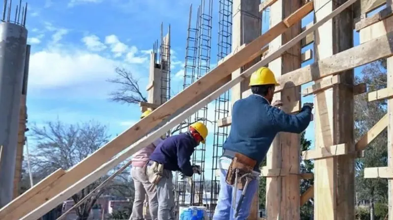 Obreros con cascos de seguridad trabajando sobre vigas y columnas en una obra en construcción.