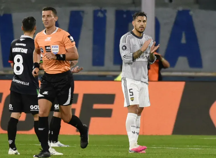 Leandro Paredes aplaude en una cancha de futbol cerca de un arbitro con camiseta naranja y otro jugador.