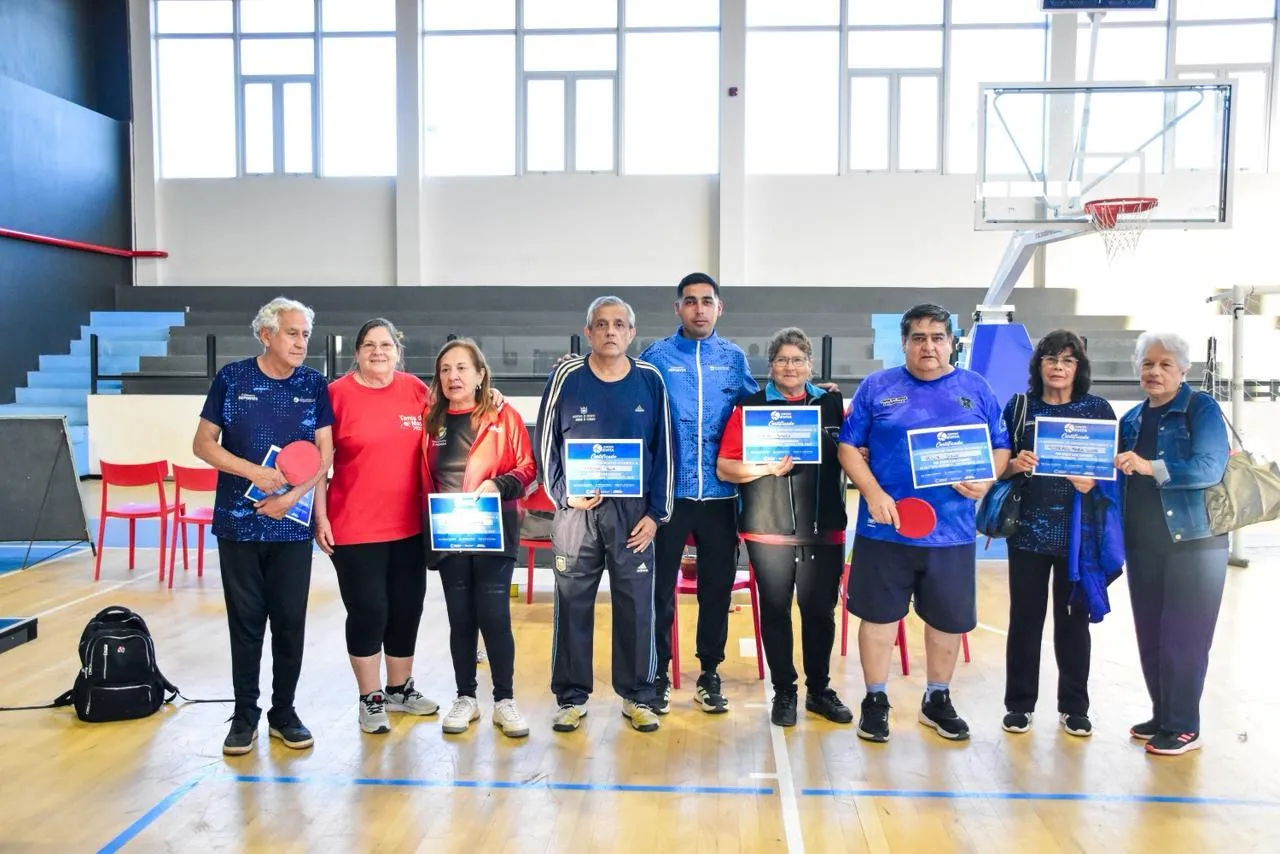 Un grupo de ocho personas posa parado en una cancha de básquet sosteniendo paletas de pimpón y diplomas.