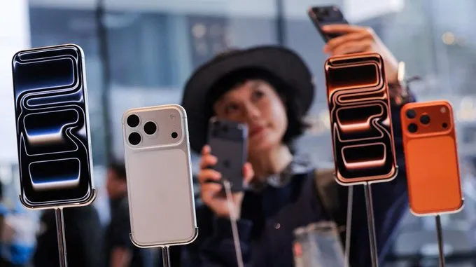 Una persona con sombrero saca una foto con su celular detrás de teléfonos exhibidos en soportes metálicos.