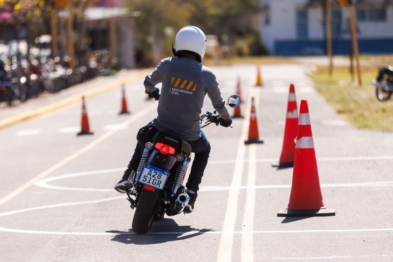 Una persona con casco conduce una moto entre conos anaranjados sobre una pista asfaltada.