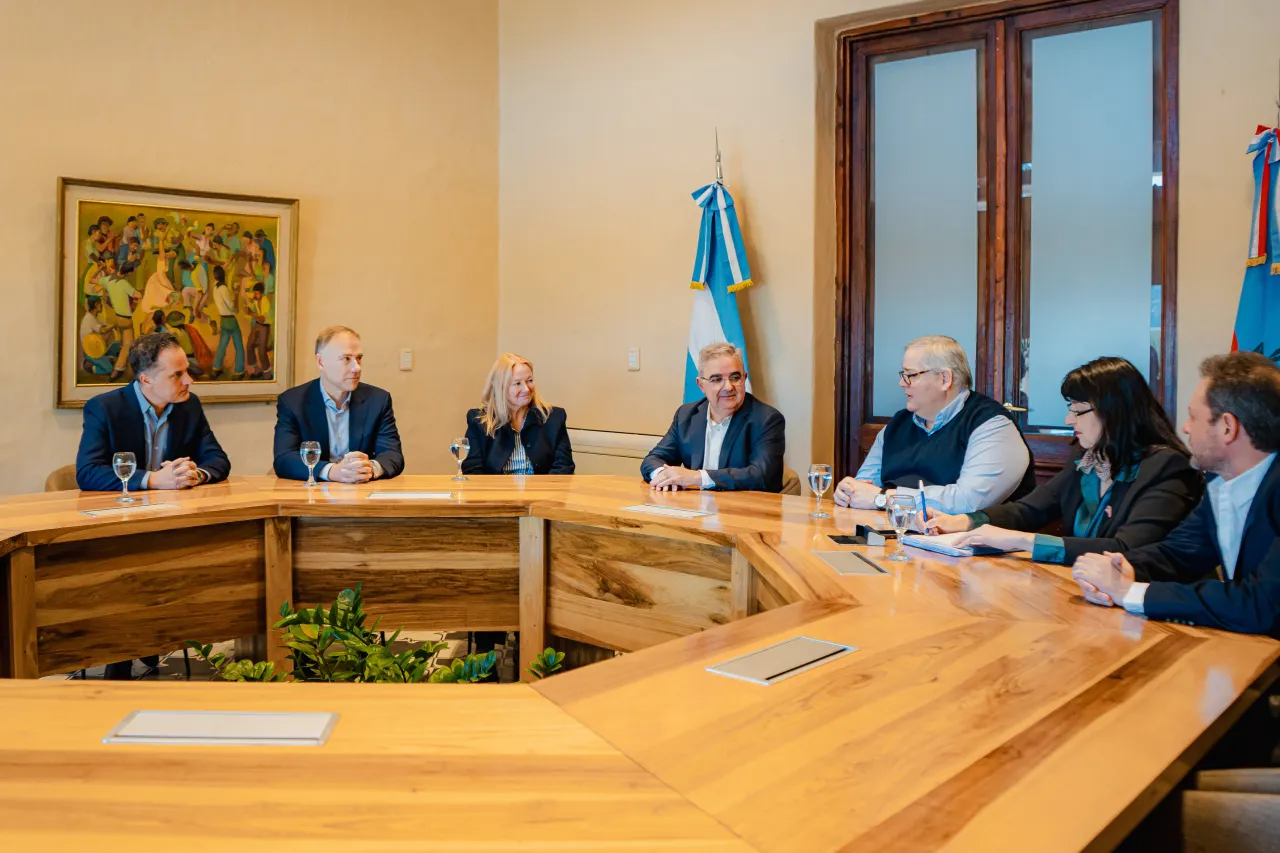 Raúl Jalil encabeza una reunión con funcionarios y empresarios sentados alrededor de una mesa redonda de madera.