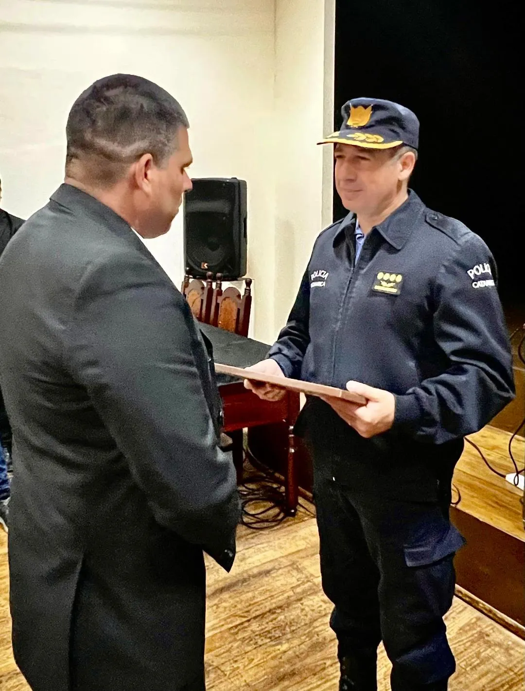 Un hombre de traje le entrega una placa o cuadro a un policía uniformado.