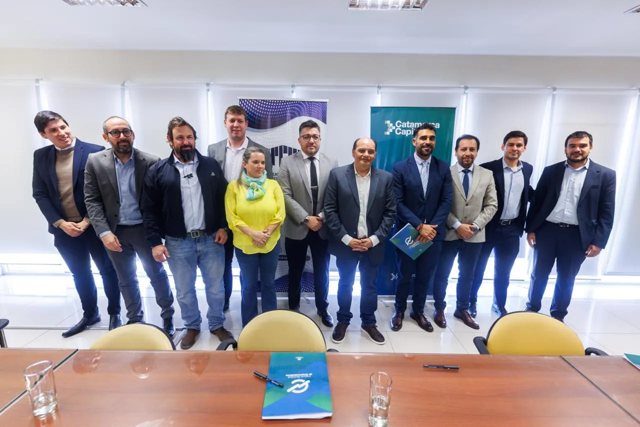 Un grupo de personas posa de pie en una sala junto a una mesa de reuniones y carteles institucionales.