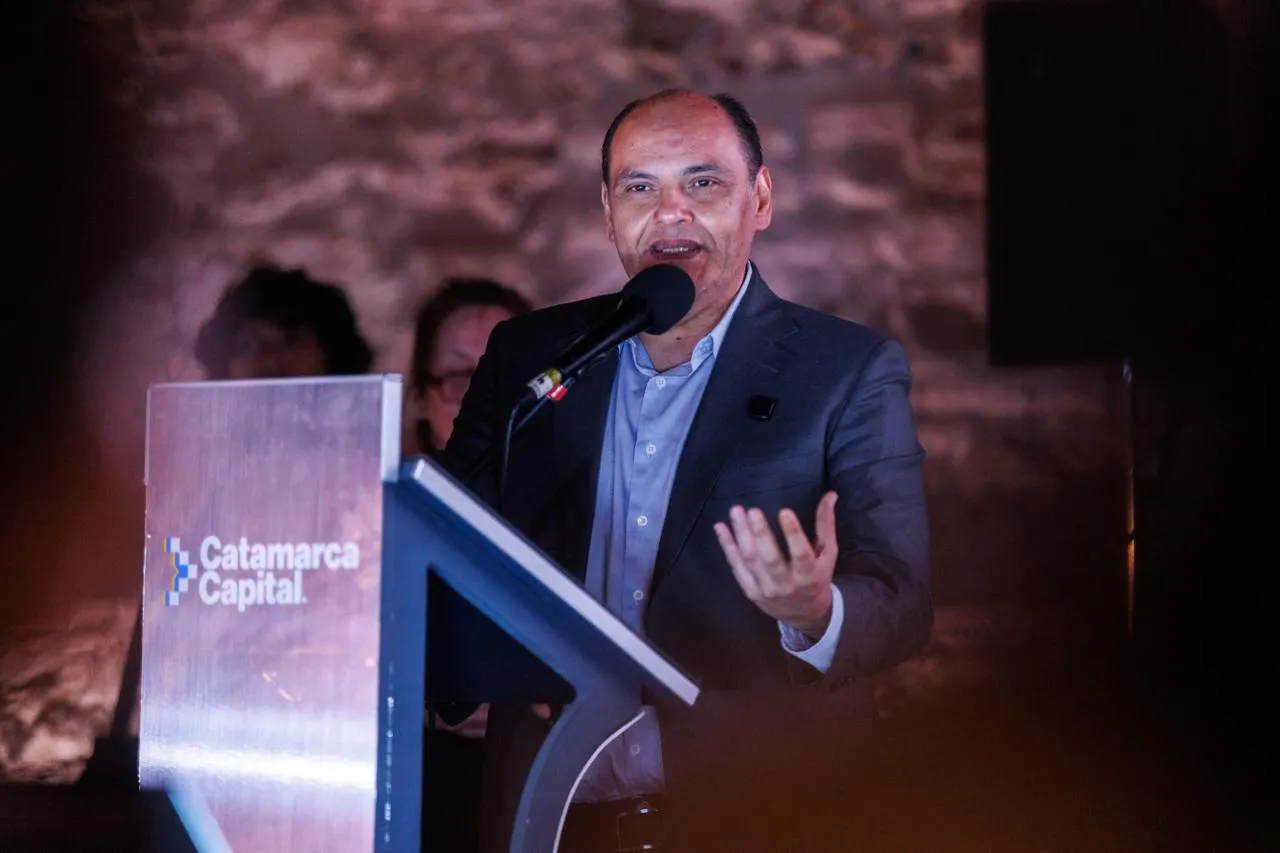 Gustavo Saadi habla frente a un micrófono en un atril con la inscripción Catamarca Capital.