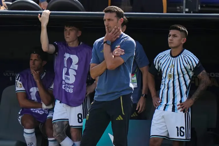 Lionel Scaloni parado junto a jugadores en el banco de suplentes de la selección argentina.