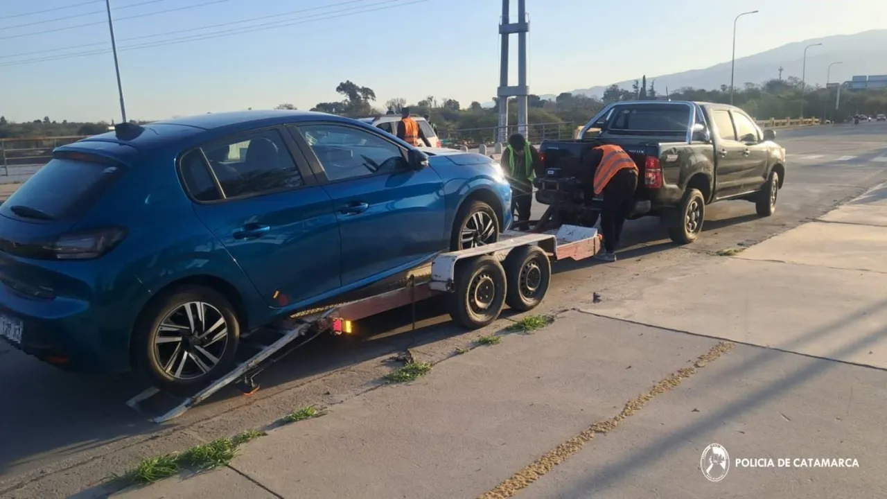 Un auto azul está subido a un trailer enganchado a una camioneta mientras varias personas trabajan alrededor.