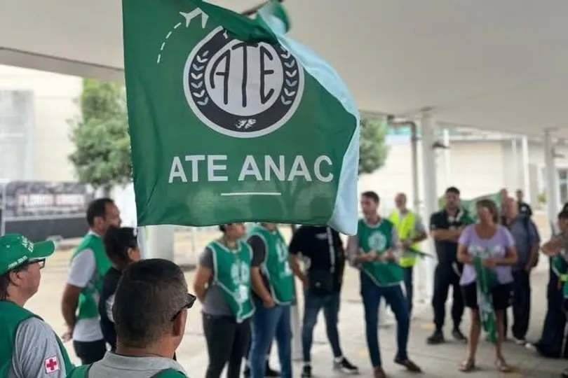 Una bandera verde de ATE ANAC flamea en primer plano frente a un grupo de trabajadores reunidos.