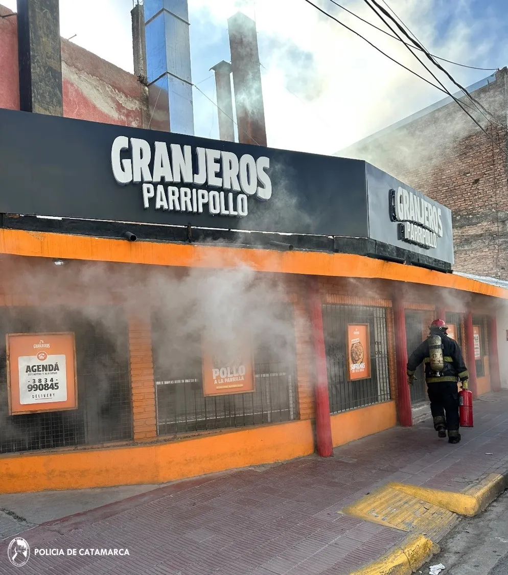 Un bombero con matafuego camina por la vereda frente a una rotisería con humo saliendo de la fachada.