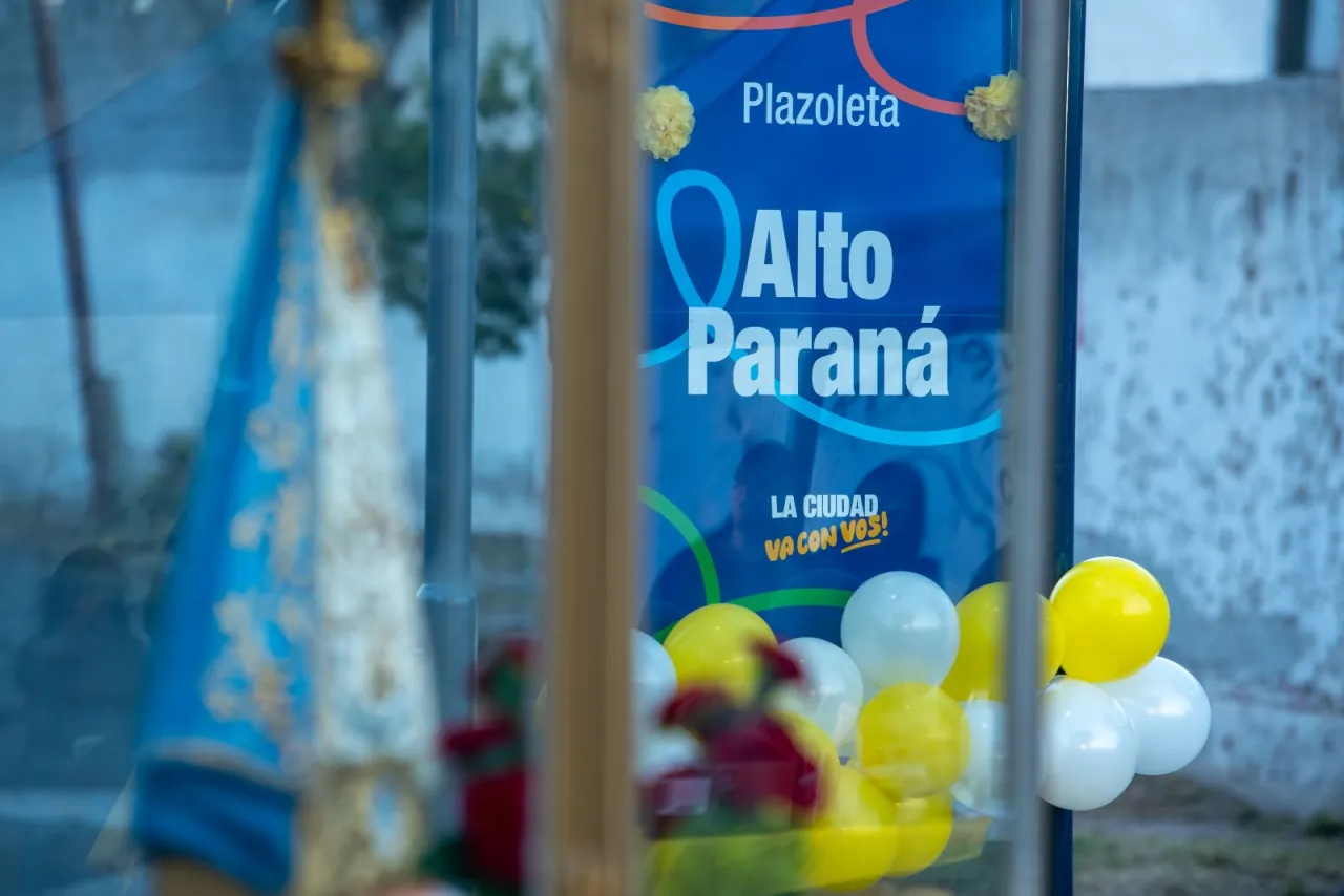 Un cartel de la plazoleta Alto Paraná decorado con globos amarillos y blancos frente a una gruta.