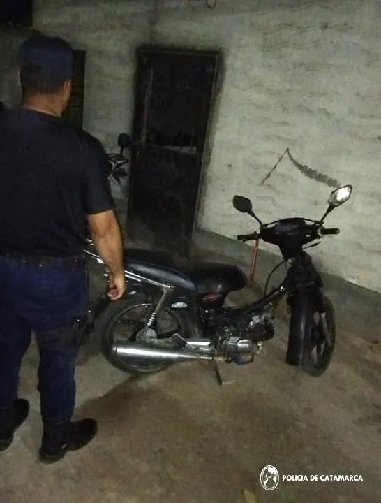 Un efectivo policial parado junto a una motocicleta 110 cc negra apoyada en su soporte.