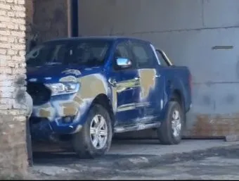 Una camioneta azul con parches de masilla beige en la chapa está estacionada junto a una pared.
